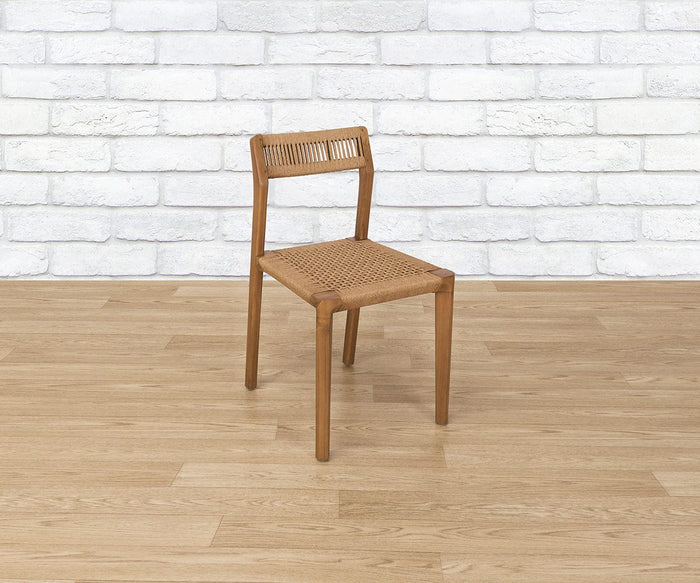The Pablo Dining Chair, featuring a woven seat and backrest, is placed on a light wood floor in front of a white brick wall.