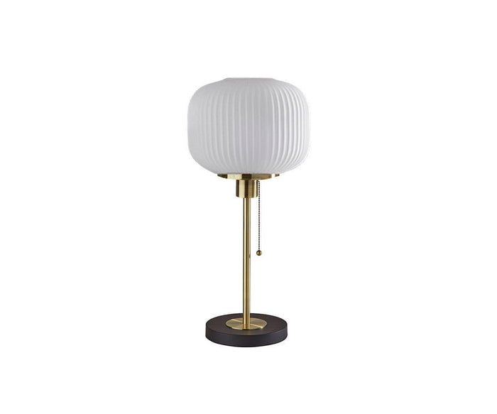 The Patina Table Lamp features a round, fluted pattern frosted glass lampshade, a brass stand, and a black circular base with a convenient pull chain switch. Shown here in the Black/Brass colorway against a white background.