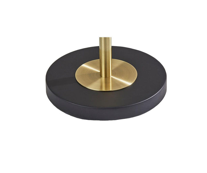 A close-up of the Patina Table Lamp showcases its round base with a black circular bottom, a gold cylindrical pole rising from the center, and a frosted glass lampshade that adds an elegant touch.