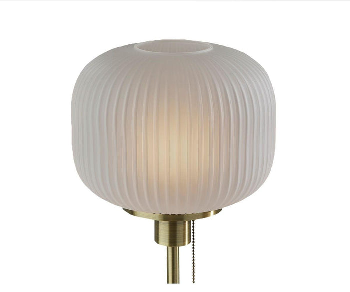 The Patina Table Lamp features an elegant fluted frosted glass shade and a brass base. When switched on, it emits a soft, warm glow through its refined lampshade, with a pull chain hanging from the fixture for easy operation.
