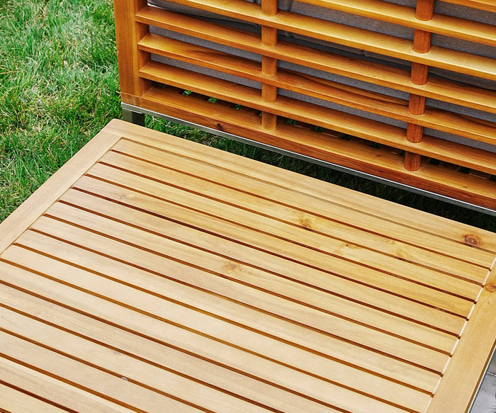 Close-up of the Playa Mar Outdoor Coffee Table, featuring light-brown horizontal wooden slats with a sleek teak finish, placed on green grass. The image highlights the texture and pattern of the slatted design.