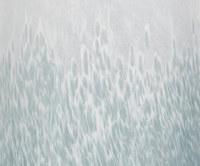 A close-up of a textured white and pale blue surface, reminiscent of cascading water and abstract frost, with elongated oval forms blending vertically—evoking the artistry of the Polar Frost Vase and its hand-finished ombré design.