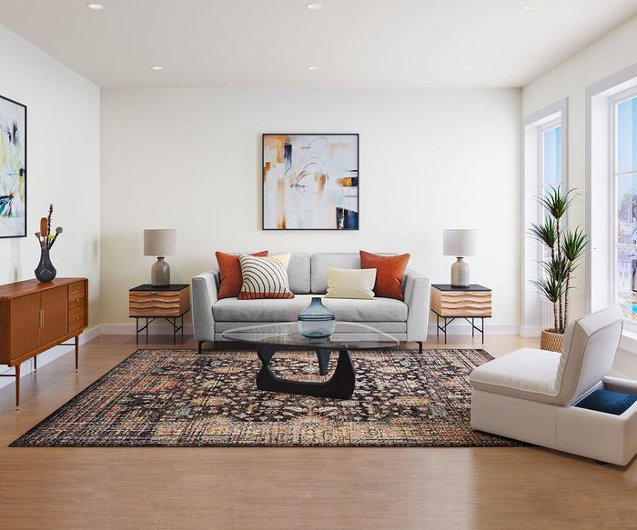 A bright, modern living room featuring a grey sofa with orange and white throw pillows, a large dark patterned rug, a mid-century modern wood sideboard, matching end tables with Polished Terracotta Lamps topped with fabric lamp shades, abstract wall art, and a white accent chair by the window.
