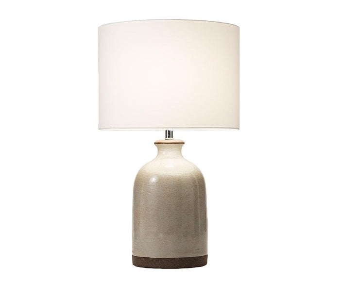 The Polished Terracotta Lamp features a round, ceramic beige base and a large white fabric lampshade, beautifully illuminated against a plain white background.
