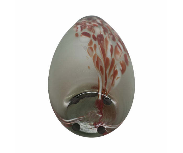 The Poppy Frost Vase is a hand-finished glass piece shaped like an egg, featuring a frosted surface with swirling red and cream patterns reminiscent of subtle floral accents, and designed to rest on its side with three black circular pads on the bottom.