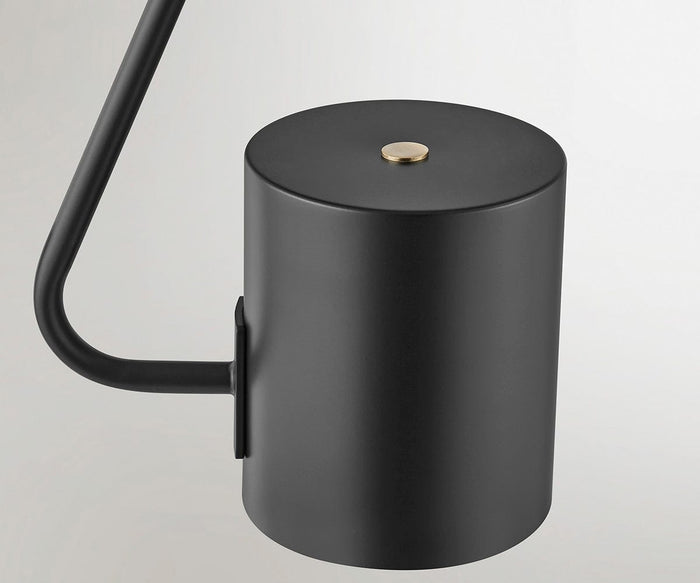 A close-up of the Quade Floor Lamp, highlighting its minimalist modern design with a black metal cylindrical body, a gold button accent on top, and a slender black arm set against a plain light background.