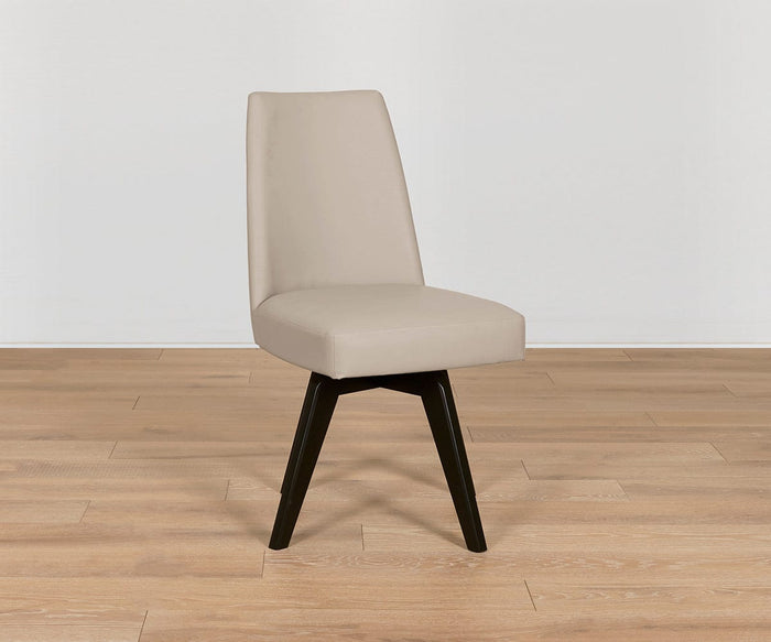 The Raynor Leather Swivel Dining Chair, featuring angled beech legs and modern upholstery, sits on a light wood floor against a plain white wall.