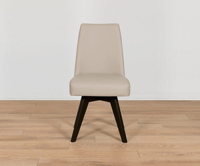 The Raynor Leather Swivel Dining Chair, featuring a modern beige upholstered seat, high backrest, and dark beech legs, sits on a light wood floor against a plain white wall.