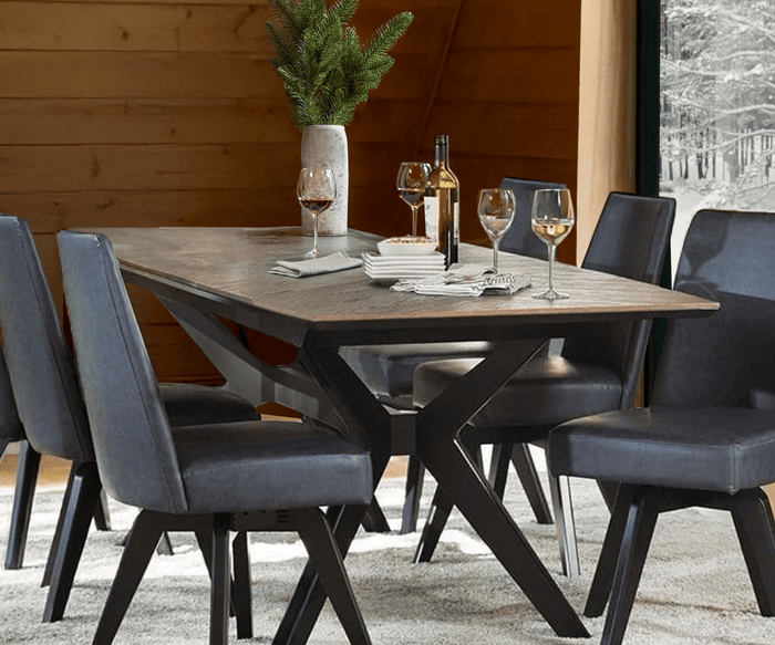 A modern dining table with six Raynor Swivel Dining Chairs upholstered in dark blue, wine glasses, a wine bottle, plates, and a tall vase with greenery. A window shows a snowy landscape outside.
