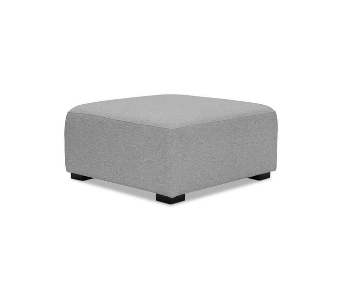 A square Reyes Ottoman in light gray, showcasing durable upholstery and plush cushioning, sits on short black legs against a white background.