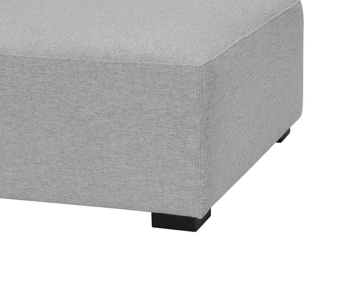 A close-up of the corner of the Reyes Ottoman, featuring light gray upholstery, plush cushioning, and black rectangular feet against a white background.