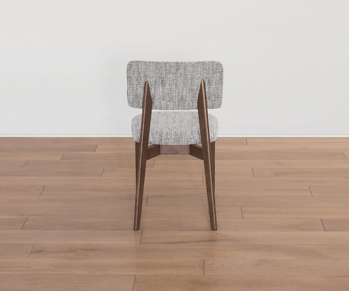 The Saga Dining Chair, featuring a light gray upholstered seat and backrest, is pictured from behind on a light brown wooden floor against a plain white wall, exemplifying timeless mid-century style.