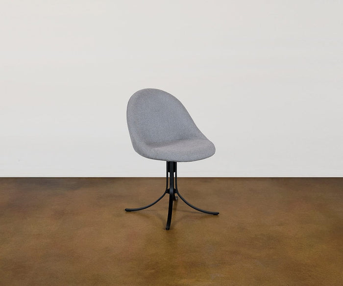 A Selene Dining Chair, featuring modern gray upholstery, a rounded backrest, and sleek black metal legs, is positioned on a brown floor against a plain white wall.