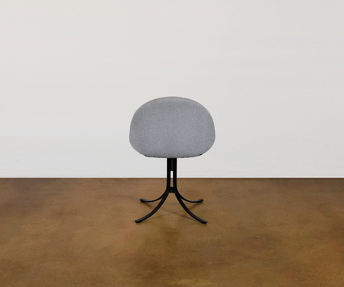 The Selene Dining Chair, featuring a modern gray design with a rounded backrest and sleek black metal legs, is pictured from behind on a brown floor against a simple white wall—this contemporary piece seamlessly combines style and comfort to enhance any dining area.