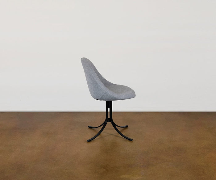 The Selene Dining Chair, featuring modern gray upholstery, a curved backrest, and a black metal four-legged base, sits on a brown floor against a plain white wall. This contemporary piece delivers both comfort and sophisticated style to any interior setting.