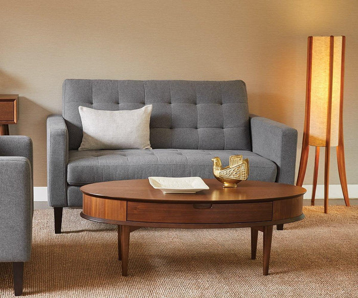 A gray tufted sofa with a light pillow, a wooden coffee table adorned with a gold bird decor and dish, and the Sendai Floor Lamp featuring its distinctive wooden base rest on a beige carpet in the modern living room, enhancing the space’s refined contemporary design.