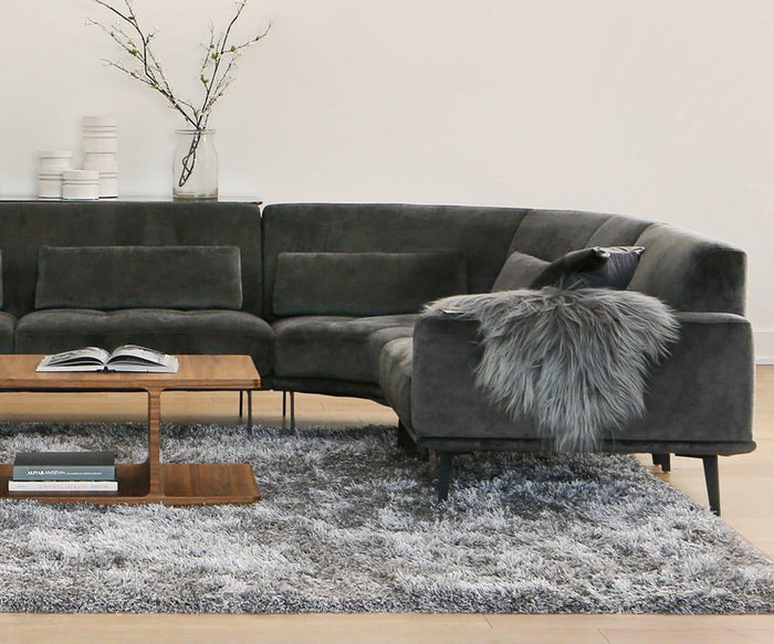 Modern living room with a dark gray sectional sofa, a Sheepskin Throw - Grey, a wooden coffee table with books, a Scandinavian rug in soft gray tones, and minimalist decor including vases with branches on a white wall.