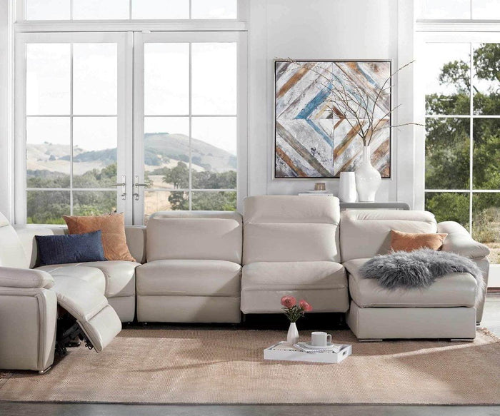 A modern living room with a white sectional sofa, colorful cushions, a grey Sheepskin Throw, a tray with flowers and books, large windows showing a scenic view, and a geometric art piece on the wall.