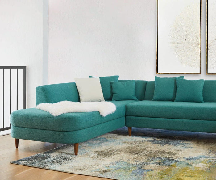 A teal sectional sofa with matching cushions and a white throw blanket sits on a multicolored rug in a bright room with light walls and two abstract wall art pieces, completed by the Sheepskin Throw - Ivory—a cozy Scandinavian essential crafted from New Zealand wool.