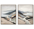 The Shoreline Drive I & II Wall Art Set features two framed landscape paintings that depict winding roads through hills beside a body of water, rendered in muted earth tones and soft, abstract brushstrokes. This multi-colored coastal wall art on textured canvas evokes the tranquil charm of a serene shoreline scene.