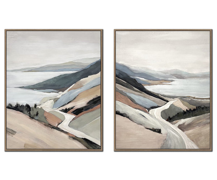 The Shoreline Drive I & II Wall Art Set features two framed landscape paintings that depict winding roads through hills beside a body of water, rendered in muted earth tones and soft, abstract brushstrokes. This multi-colored coastal wall art on textured canvas evokes the tranquil charm of a serene shoreline scene.