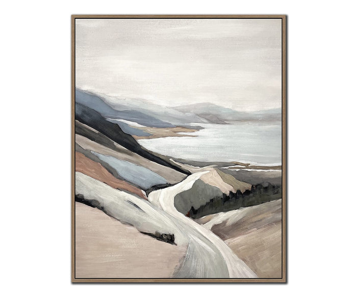 The Shoreline Drive I & II Wall Art Set features framed paintings of a winding road leading toward a calm lake, with mountains and hills rendered in soft, muted tones of beige, blue, and gray beneath a cloudy sky—these serene pieces of coastal wall art beautifully capture the tranquil ambiance of nature’s untouched beauty.