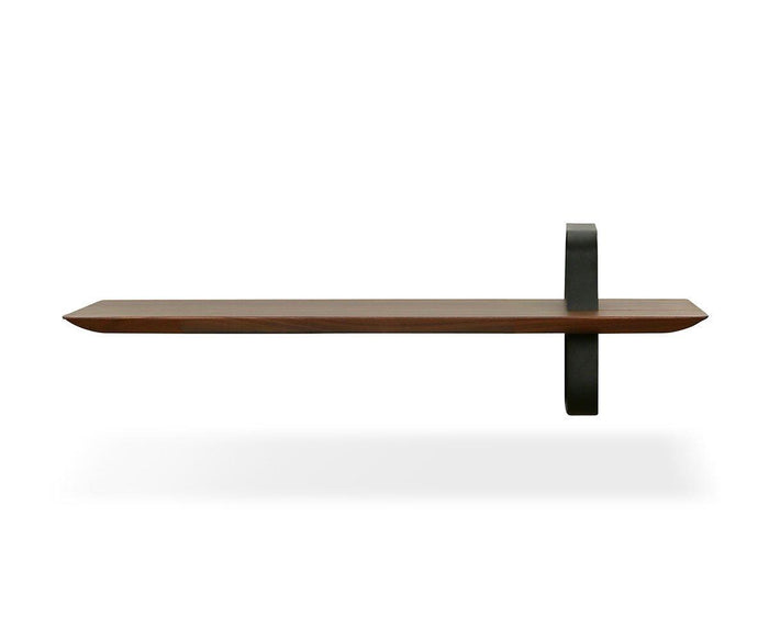 The Sigra Shelf is a minimalist wooden wall shelf in walnut, featuring an asymmetrical design with a single black metal support loop on the right side, displayed against a white background.
