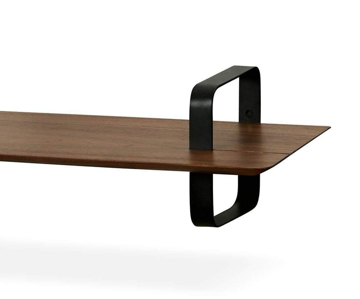 The Sigra Shelf is a rustic industrial piece, featuring a wooden design with black metal brackets that loop over and under one end, creating a striking silhouette against a white background.