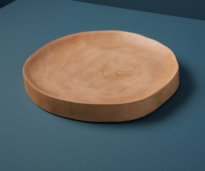 The Sindri Mango Wood Platter, featuring a round and flat design with natural mango wood grain, rests on a blue surface. Its uneven edges lend a rustic, handcrafted look inspired by Thailand and emphasize its sustainable wood origins.