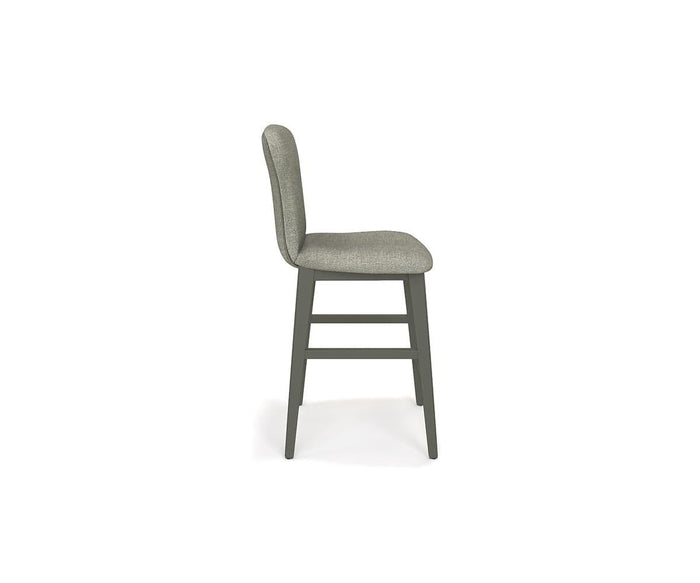 A side view of the Slater Bar Stool highlights its modern charm with a cushioned gray seat and backrest. This elegant bar stool is supported by four dark wooden legs, connected at the base by two footrests. The simple yet sophisticated design makes the Slater Bar Stool an ideal choice for contemporary interiors.