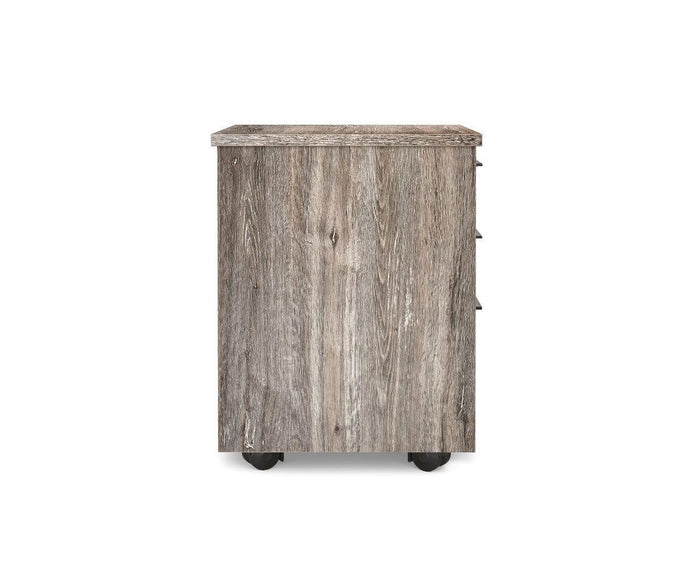 A side view of the Slater Mobile Pedestal showcases its rustic wooden finish and distinct wood grain, set on four black wheels. This mobile file pedestal features three partially visible drawer handles on the right side.