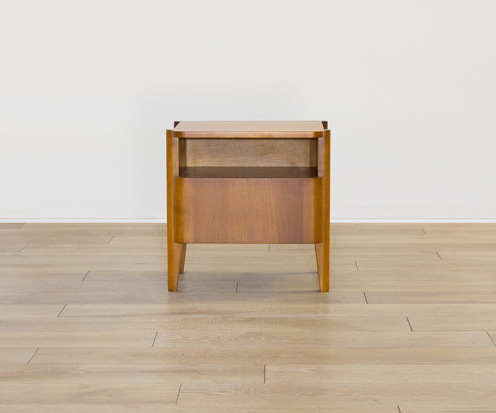The Stefan Nightstand, a Scandinavian-inspired wooden side table, features a single drawer and an open shelf below. It is shown set on a light-colored wood floor against a plain white wall.