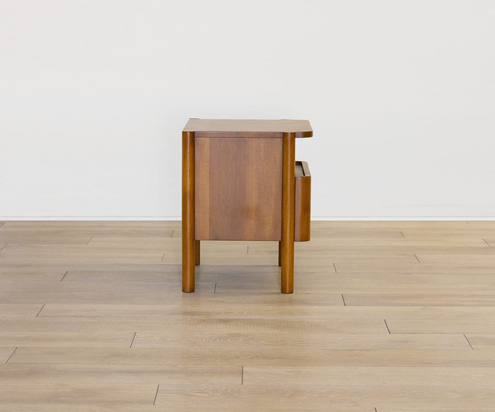 The Stefan Nightstand is viewed from the side, showcasing its smooth, flat surface and clean lines as it stands on a light wood floor against a plain white wall.