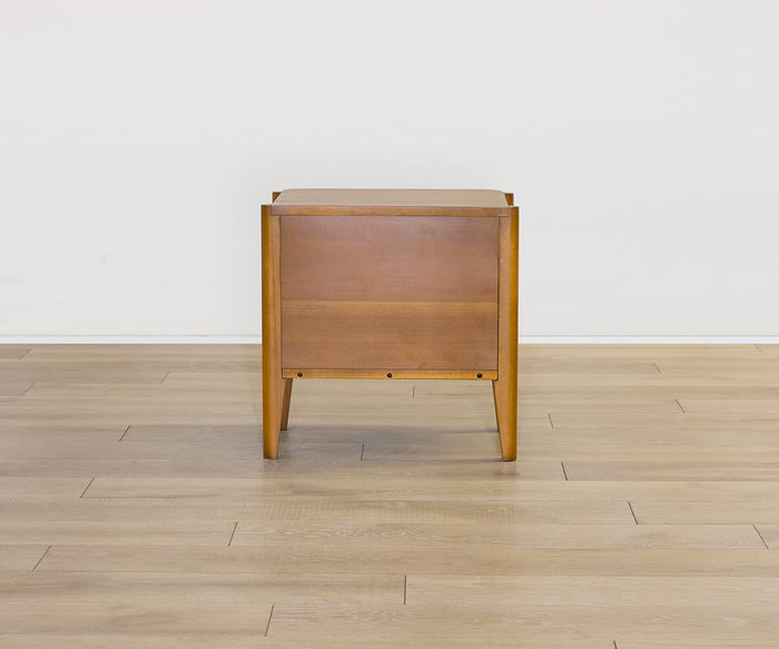 The Stefan Nightstand, featuring clean mid-century lines, sits on a light wood floor against a plain white wall and is viewed directly from the side.