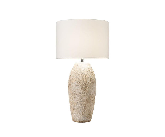Introducing the Stone Shores Table Lamp - Tall, a rustic table lamp distinguished by its textured, beige stone-like base and minimalist cylindrical white lampshade. Perfect for modern home decor, this striking piece makes a statement against any plain white background.