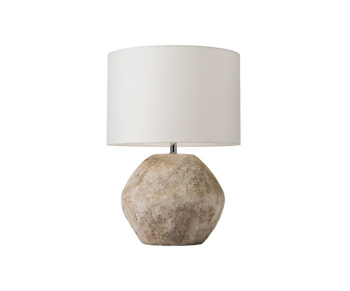 The Stone Shores Table Lamp features a textured, stone-like round base in stone white and a simple white cylindrical lampshade, making it perfect for adding warmth to modern home décor. Shown against a white background.