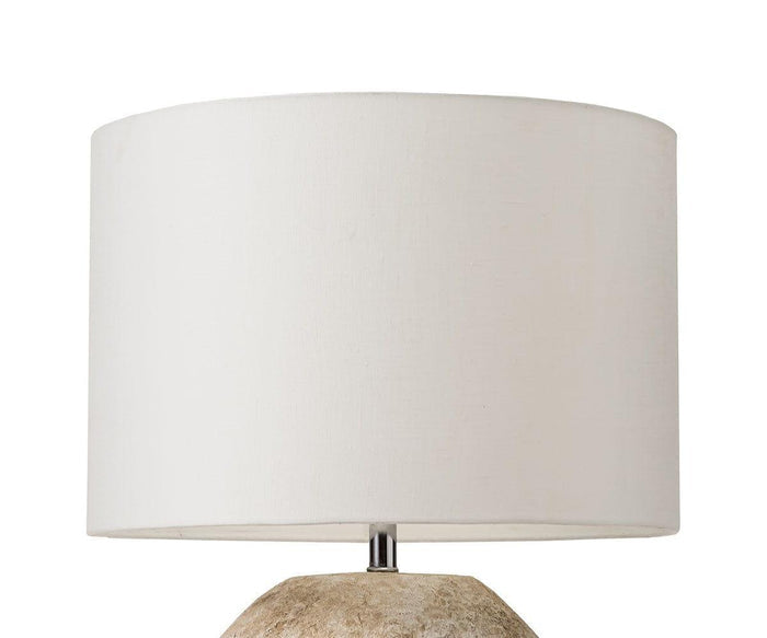 A close-up of the Stone Shores Table Lamp, featuring a round white fabric lampshade and a beige, textured base against a white background—an ideal piece for adding warmth to modern home decor.
