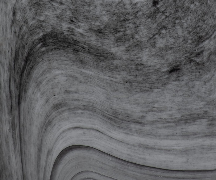 Close-up of a smooth, curved, layered rock surface in shades of gray with visible striations and subtle texture variations, reminiscent of the marbled pattern featured in the hand-finished glass artistry of the Stormy Swirl Vase.