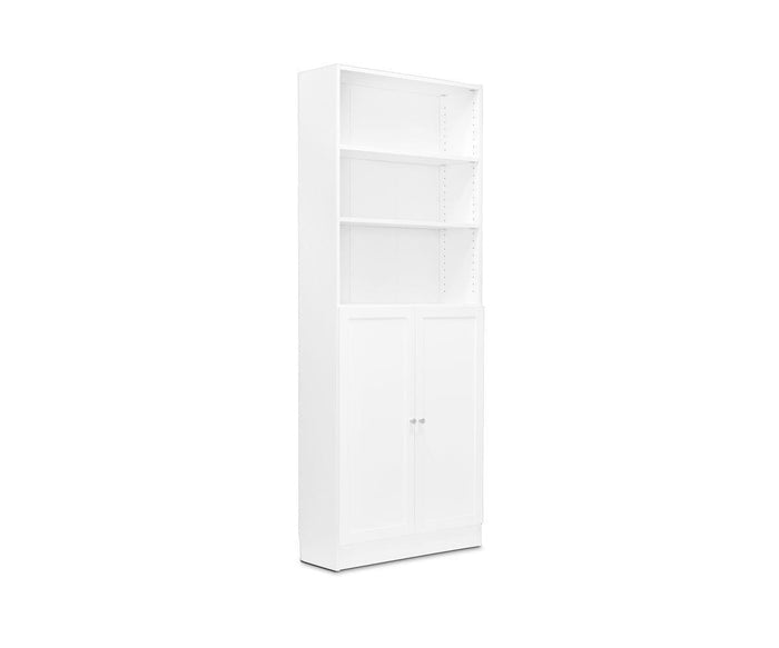 The Stuen Narrow Panel Door bookcase features a tall white design with two open shelves on top and a closed cabinet with panel doors at the bottom, providing a stylish storage upgrade and shown against a plain white background.
