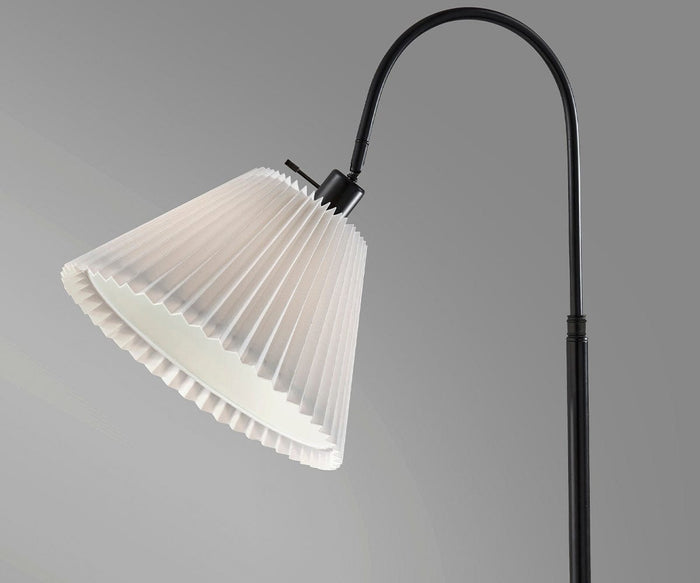 The Thalia Floor Lamp features a sleek black curved stand and a pleated white lampshade, displayed against a plain gray background.