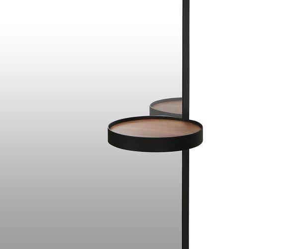 A Toive Wall Mirror reflects a round wooden shelf with a black rim, mounted on a vertical black metal rod, set against a white to gray gradient background.