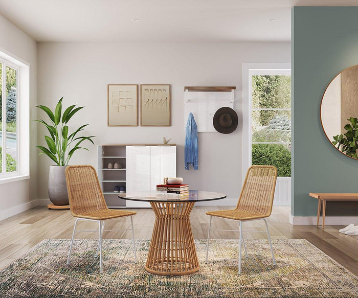 A modern, airy dining area featuring two Tori Dining Chairs arranged around a round glass table, complemented by a rug, potted plant, wall art, coat hooks adorned with a hat and jacket, all illuminated by large windows letting in natural light.