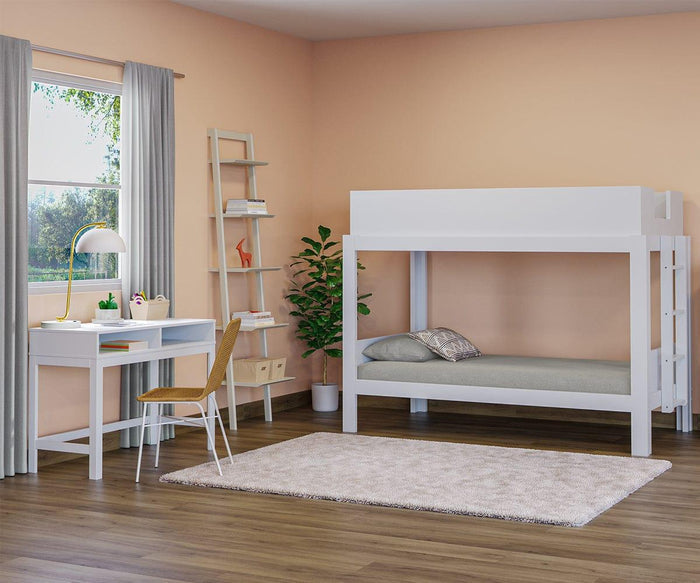 A bedroom with peach walls, a white bunk bed, a desk with a lamp and the Tori Dining Chair, a shelf with decor, a potted plant, and a beige rug on wooden flooring. Sunlight enters through a window with gray curtains.