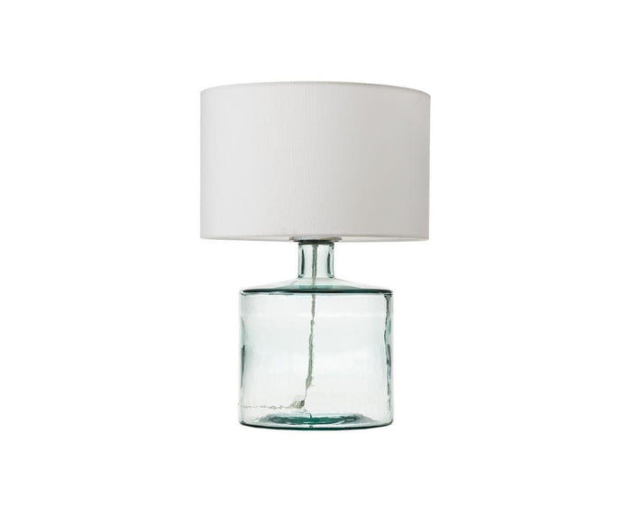 The Translucent Glass Lamp features a clear glass base and a simple white cylindrical fabric shade, displayed against a plain white background.