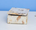 Two Tula Marble Boxes With Lid in White/Multi are stacked on a light surface, the bottom box featuring ridged detailing and the top box a smooth finish, creating a striking handcrafted decor piece against a blue background.