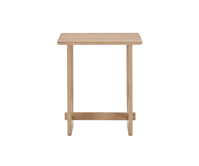 Unni Side Table in Oak—a small, square, solid oak side table from the Unni Collection featuring a simple, minimalist design with straight legs and a crossbar near the base for stability, shown against a white background.