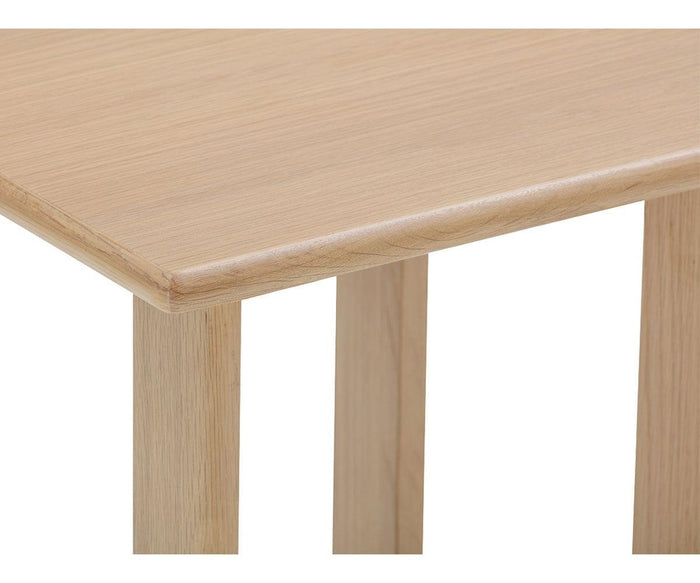 A close-up of a light wood table corner from the Unni Side Table reveals its smooth, rectangular tabletop and four straight legs below, all crafted from solid oak. This elegant mid-century piece showcases timeless design and quality materials.