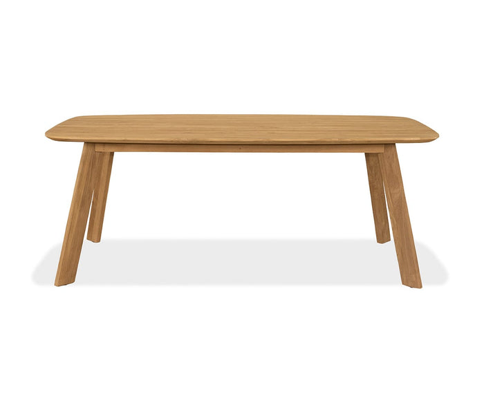 The Vinicio Outdoor Dining Table, shown in natural teak against a white background, features a rectangular wooden top with rounded edges and four angled legs. Its simple, modern design makes it an ideal choice for contemporary outdoor spaces.