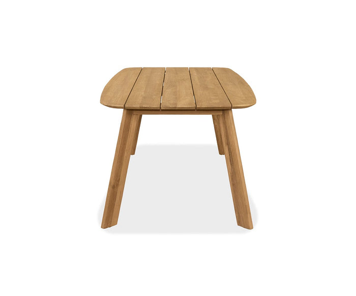 The Vinicio Outdoor Dining Table, crafted from solid teak with a natural finish, features a rectangular slatted top and four angled legs. Viewed from the short end against a white background, its sleek design and durable construction perfectly embody modern outdoor furniture style.
