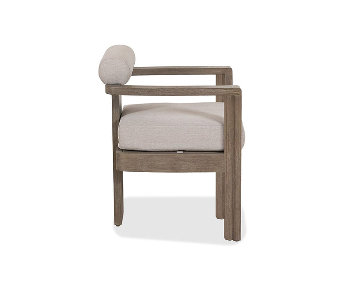 The Vinna Outdoor Dining Chair features a modern wooden frame with straight, simple lines and open armrests, complemented by a light beige cushion and cylindrical pillow. Viewed from the side, it exemplifies the elegance of contemporary outdoor furniture. Its weather-resistant design ensures lasting style and comfort for any patio or garden setting.